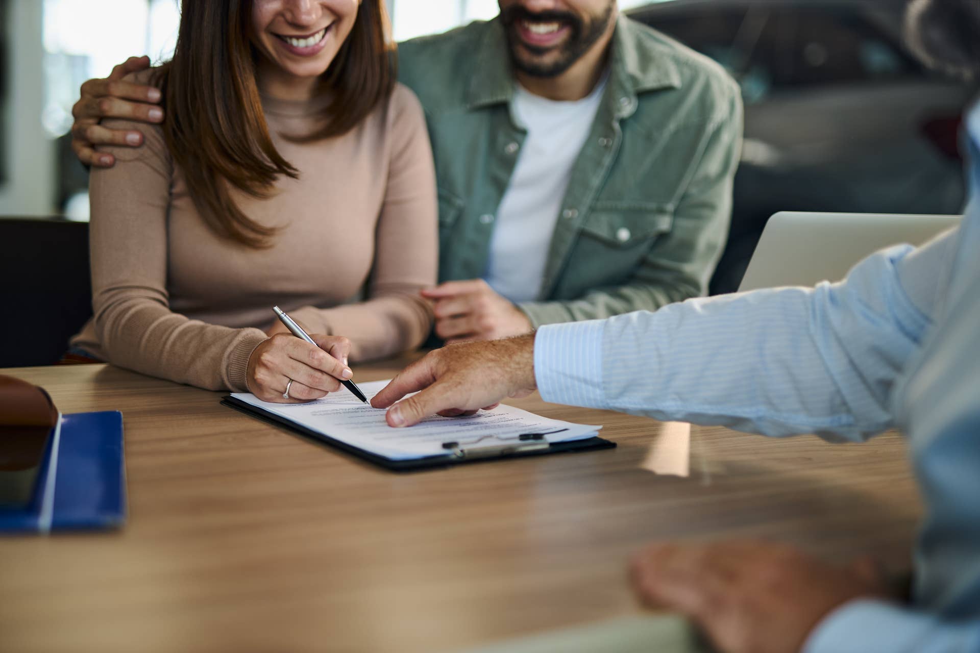 Unrecognizable young couple signing a contract for buying a car while salesman is showing them where to sign.